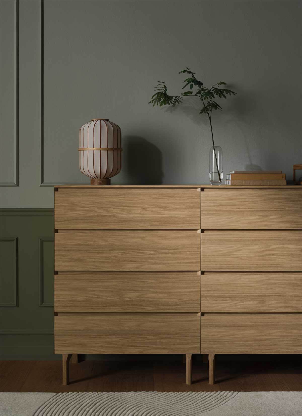 Två stycken Daia byrå med fyra lådor i vitpigmenterad ek som står bredvid varandra i ett mörkt sovrum. Byråarna är dekorerade med en lampa och en vas.