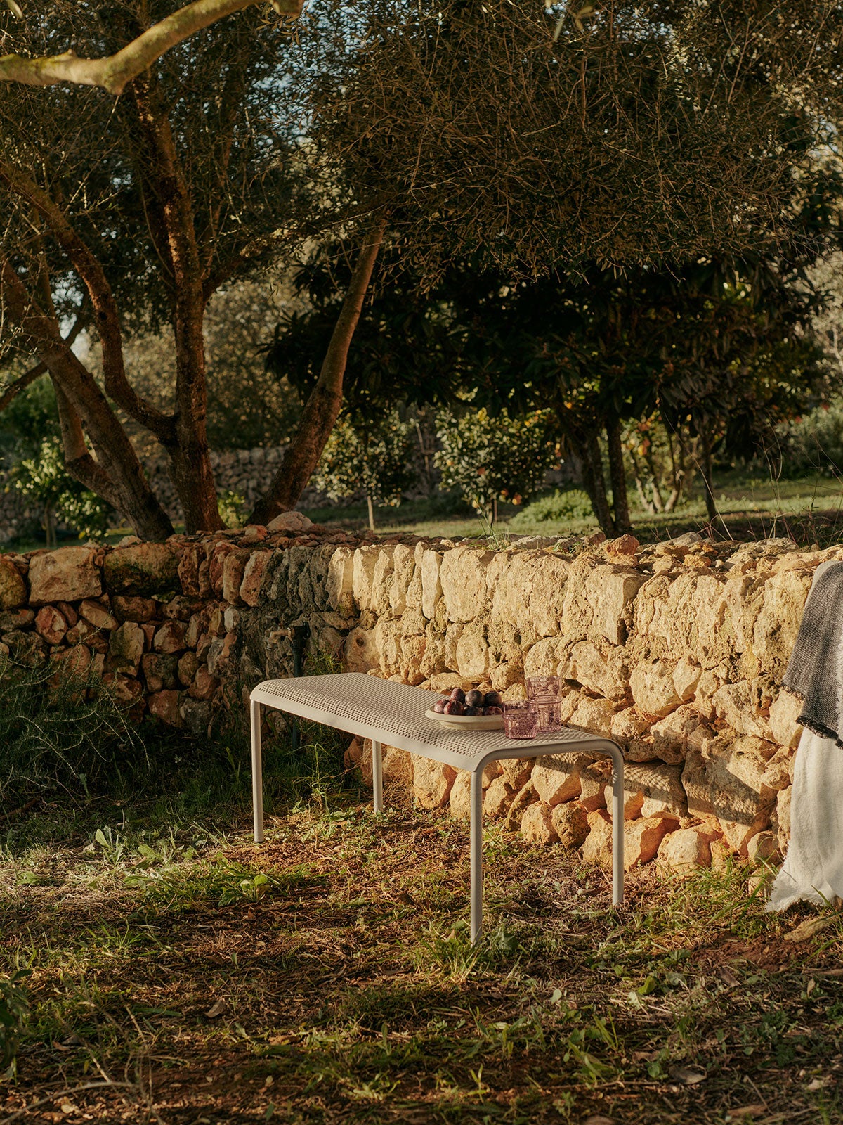 Dapple Bänk i färgen Cashmere mot en stenmur i solnedgången