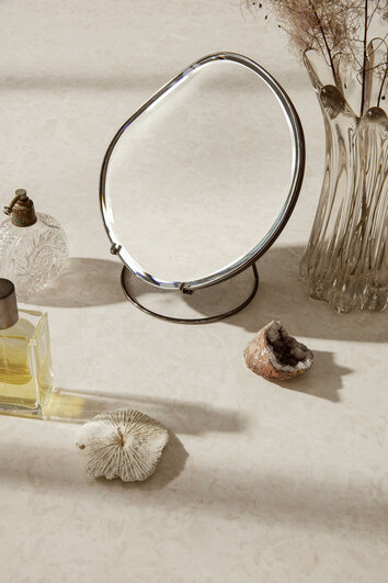 Pond Bordsspegel i utförandet Dark Chrome på sminkbord med parfymer och snäckskal