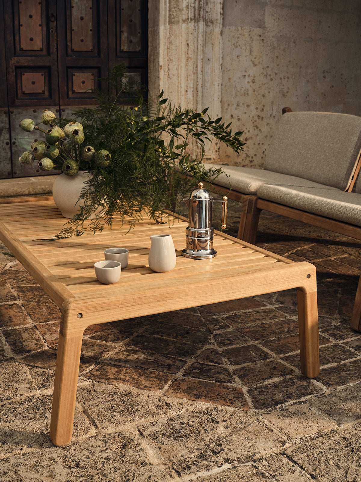 Patio soffbord 120x60 på solig uteplats. Soffbordet är dukat med kaffe, kaffekoppar och en vas med blommor.