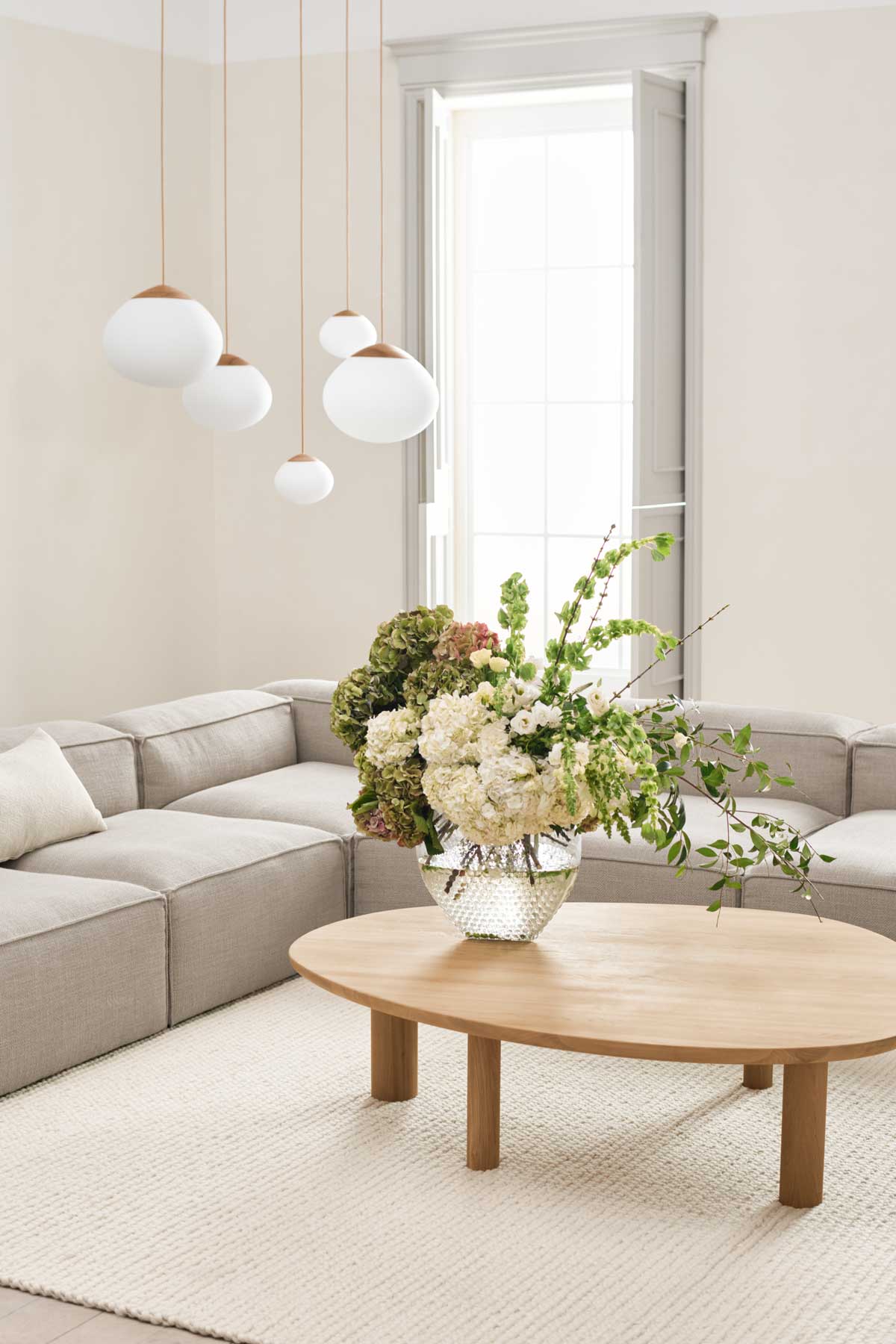 Latch soffbord i oljad ek i ett vardagsrum med en beige modulsoffa. Det står en vas med en blombukett på soffbordet.