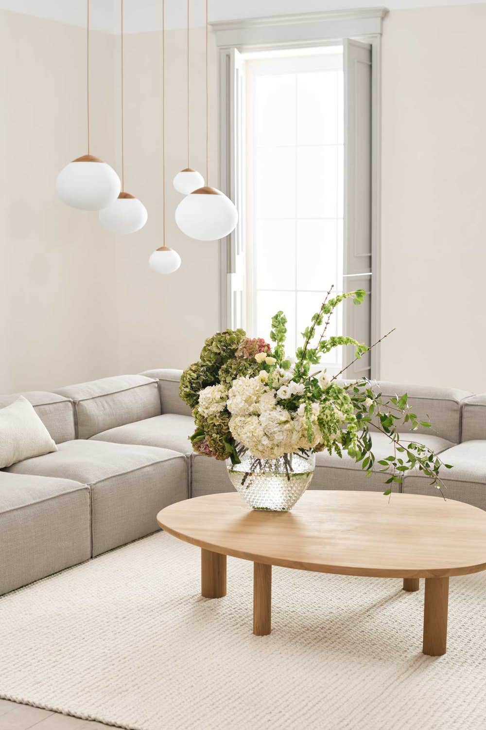 Bolia-Latch-Coffee-Table-Oiled-Oak-Lifestyle.jpg Latch soffbord i oljad ek i ett vardagsrum med en beige modulsoffa. Det står en vas med en blombukett på soffbordet.