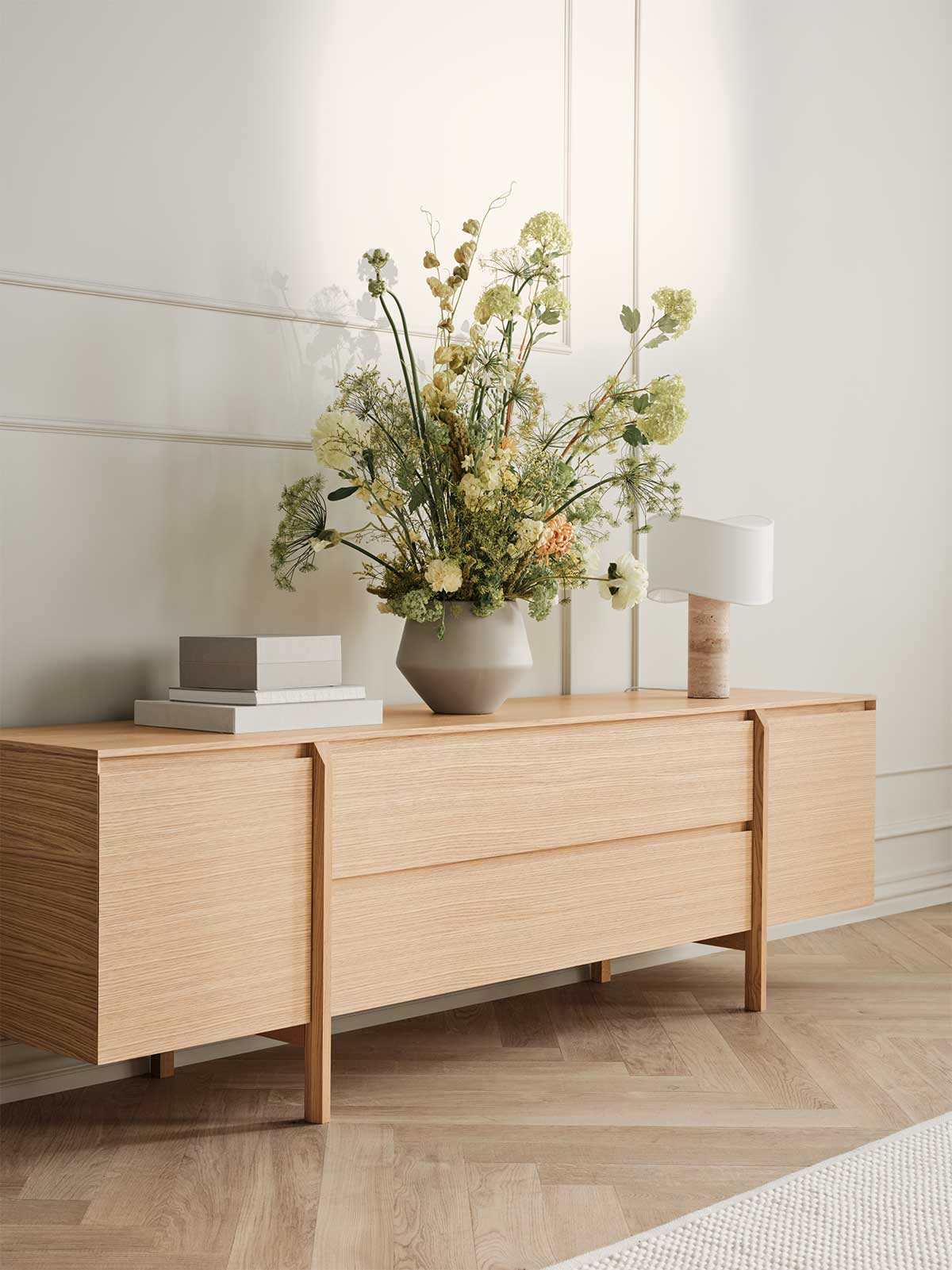 Daia Sideboard 240 med lådor i oljad ek dekorerat med böcker, en blombukett i gröna, vita och rosa toner och en lampa.