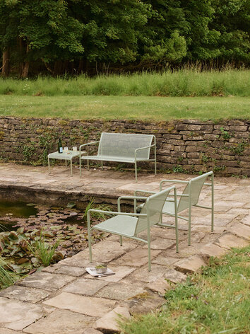 Dapple Loungesoffa och Dapple Loungebord 57x57 i färgen Tea Green som står vid sidan av en damm. På den andra sidan av dammen står två stycken Dapple Loungestol i samma färg.