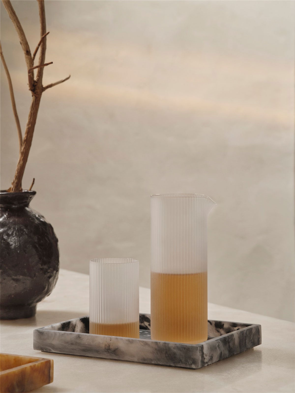 Ripple Mjölkkanna i utförandet Frosted på en marmorbricka bredvid ett fyllt glas