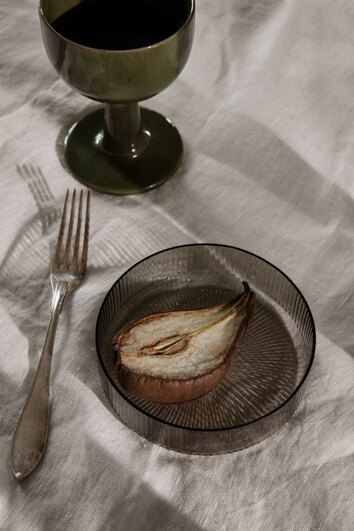 Ett päron i Ripple Skål i färgen Smoked Grey på dukat bord