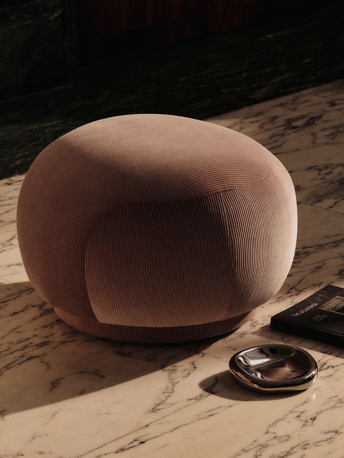 Bellure Skål i färgen Silver som står på ett stengolv bredvid en rosa sittpuff
