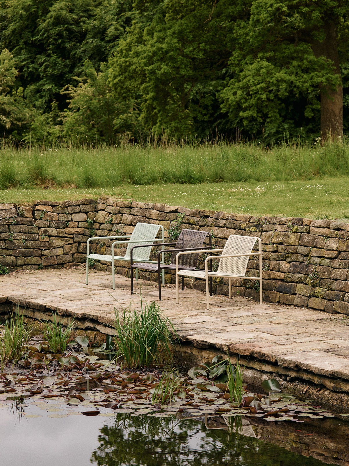 Dapple Loungestol i färgen Tea Green, Dark Chocolate och Cashmere som står på en rad bredvid en damm